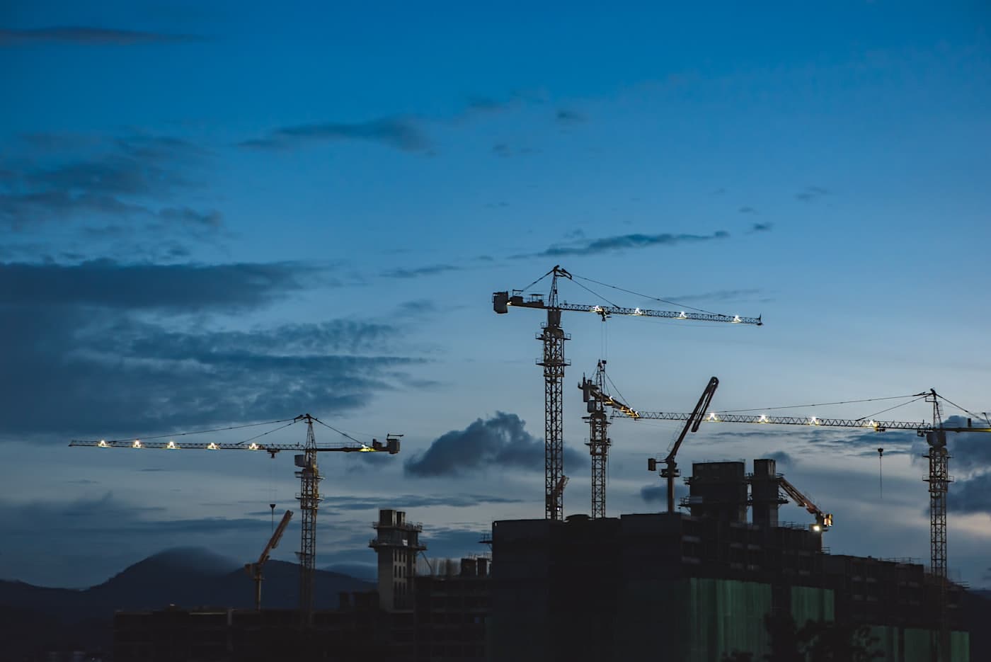 Tower cranes lit against a blue-hour sky over a construction site